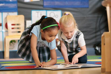 Two young students reading a book on a floor rug