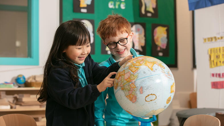 Two young students looking at a Globe